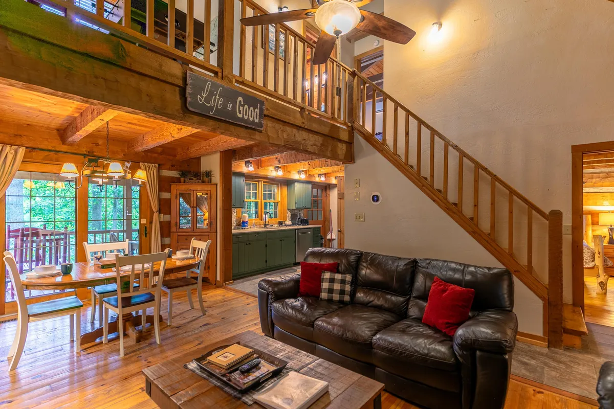 A cozy interior scene showcasing a sofa, dining table, staircase, and kitchen area immersed in natural light from large windows. The inviting layout is ideal for gathering, playing games, or relaxing after a day of exploration.