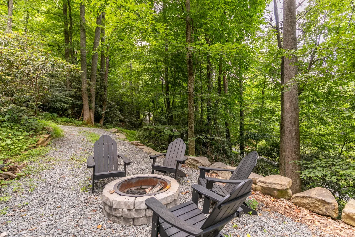 A cozy fire pit area framed by adirondack chairs and tall trees, inviting guests to gather for campfire storytelling, stargazing, or simply relaxing in the peaceful outdoors.