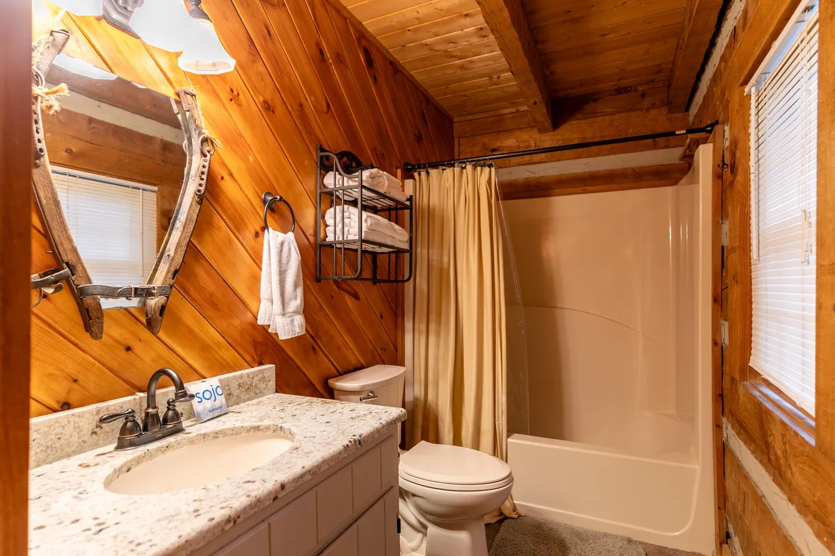 A bathroom with rustic wooden wall paneling, a granite countertop, a vintage-style mirror, and plush towels on a rack. A shower curtain hints at a full bath, creating an inviting space to refresh and unwind.