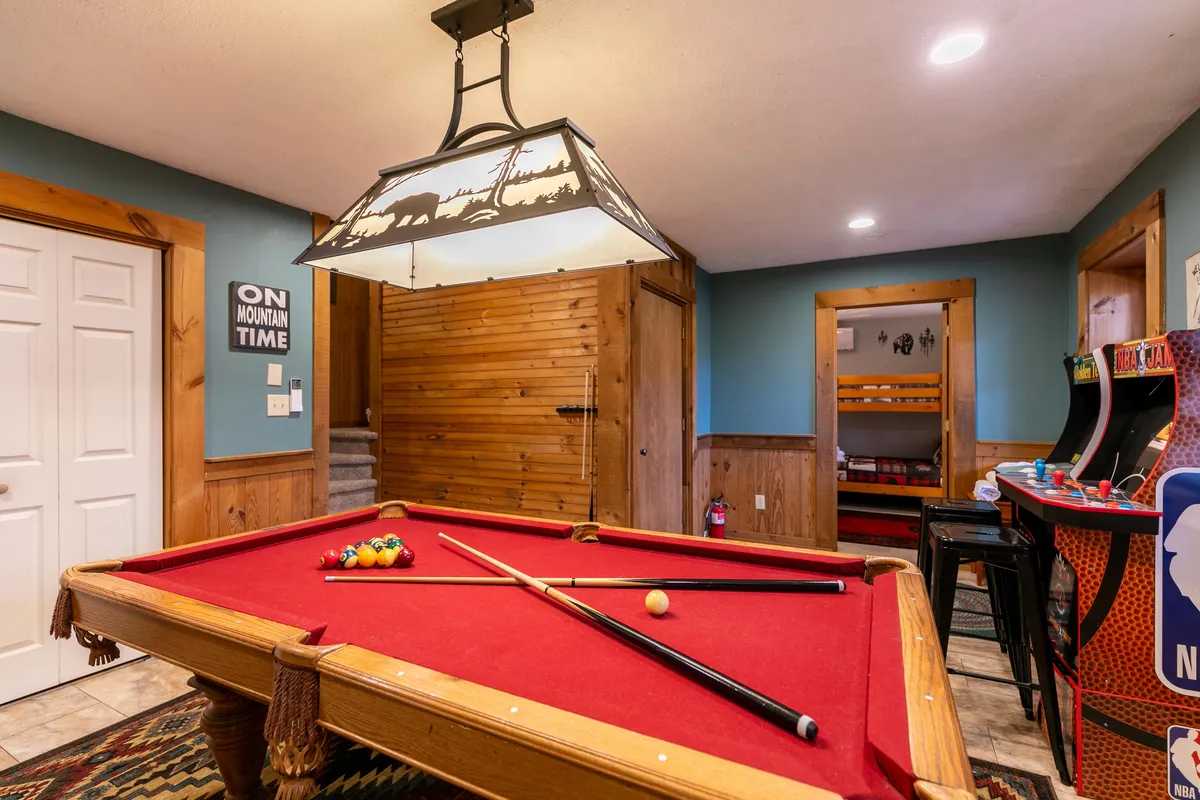 This interior shot highlights the vibrant social atmosphere of the lower level, showing the pool table, bar stools for gathering, and arcade games. The space is well-lit and arranged for group enjoyment and easy movement between activities.