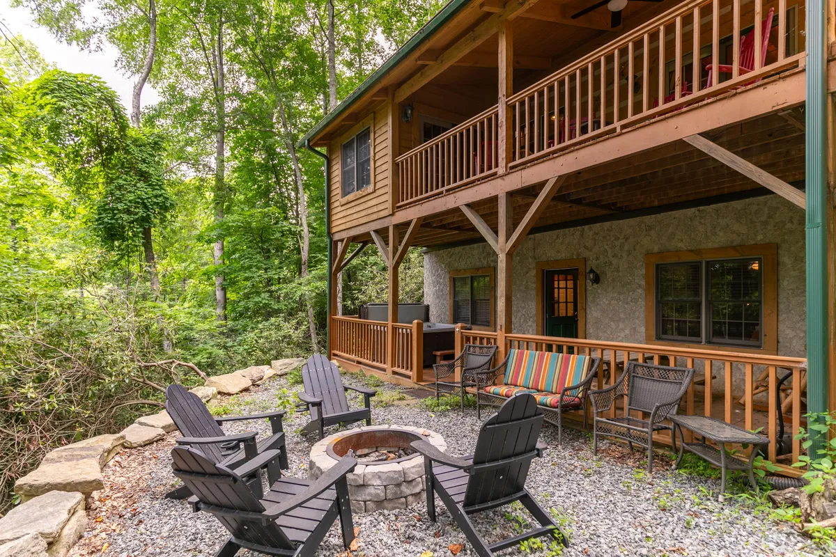 An inviting outdoor area set in a wooded environment, with a fire pit surrounded by comfortable seating and a view of a wooden balcony. The scene is designed for social gatherings, evening relaxation, and stargazing, emphasizing the cabin’s communal and adventurous spirit.