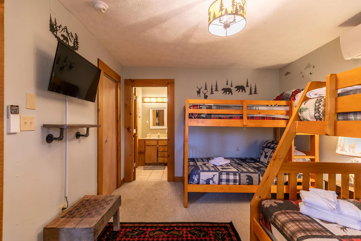 A family-friendly sleeping loft with wooden bunk beds, playful wall decor, a television, and a door leading to an adjacent bathroom. The space is inviting and designed for both rest and entertainment, suitable for children or extra guests.