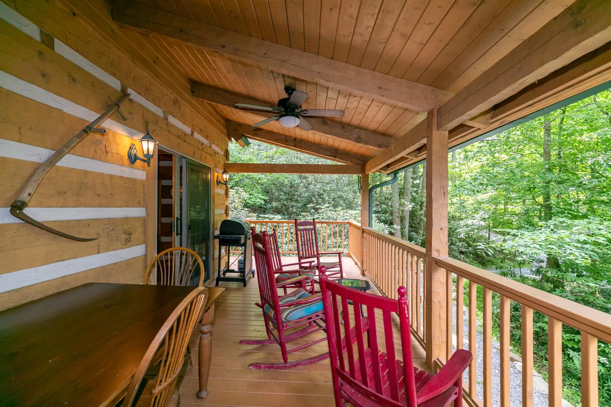 A cozy porch scene featuring rocking chairs, a wooden table, an outdoor grill, and lush greenery. The inviting setup suggests a comfortable spot for families to relax, dine outdoors, and enjoy quiet moments with pets at their side.